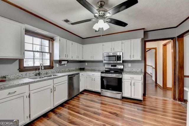 kitchen featuring hardwood / wood-style floors, white cabinetry, sink, ornamental molding, and stainless steel appliances