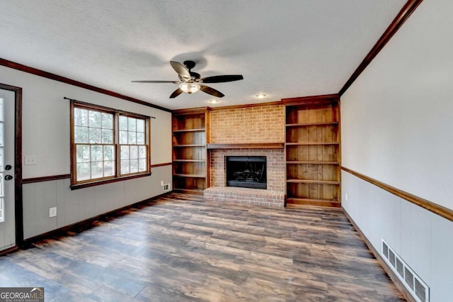 unfurnished living room with built in shelves, dark wood-type flooring, a textured ceiling, ornamental molding, and a fireplace