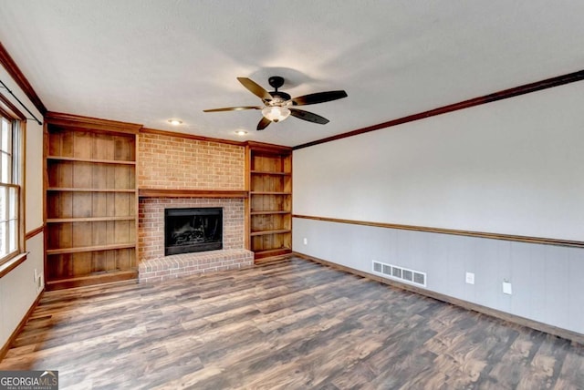 unfurnished living room with crown molding, ceiling fan, dark hardwood / wood-style flooring, a brick fireplace, and built in shelves