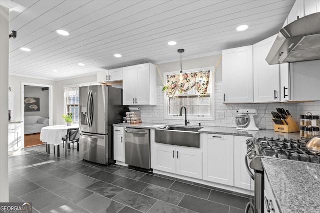 kitchen with wall chimney range hood, sink, appliances with stainless steel finishes, hanging light fixtures, and white cabinets