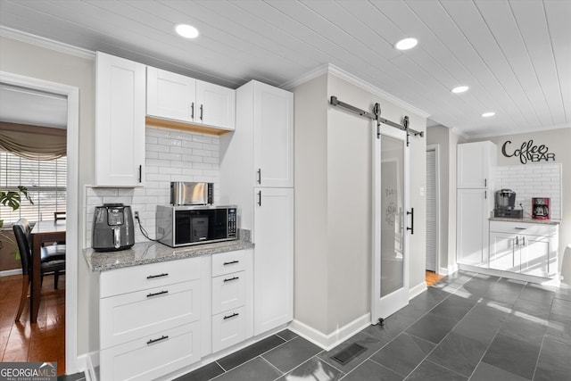 kitchen with crown molding, a barn door, white cabinets, and light stone counters