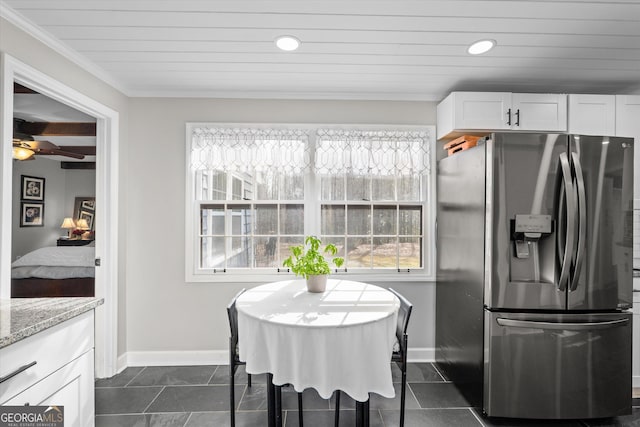 kitchen with stainless steel fridge, white cabinetry, light stone counters, ornamental molding, and dark tile patterned flooring