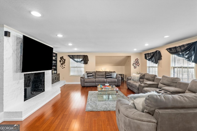 living room featuring crown molding, wood-type flooring, and a brick fireplace