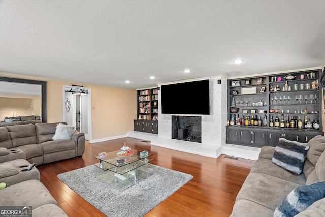 living room with dark wood-type flooring, bar area, a large fireplace, and built in shelves