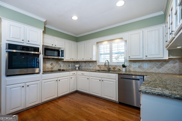 kitchen with sink, crown molding, appliances with stainless steel finishes, white cabinetry, and dark stone counters