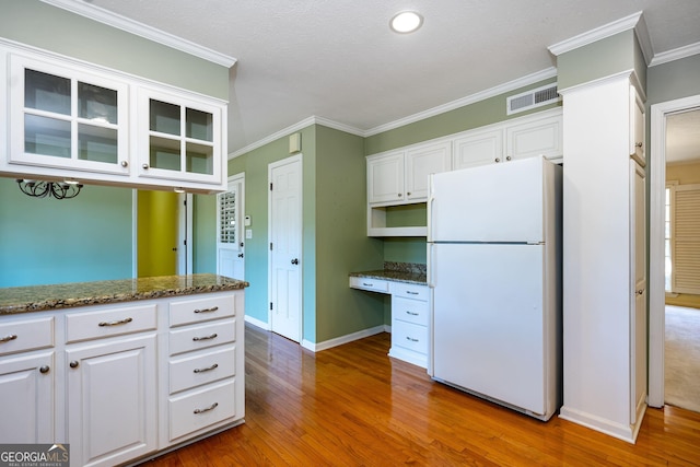 kitchen with built in desk, white cabinetry, dark stone countertops, ornamental molding, and white fridge