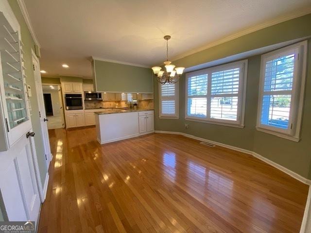 kitchen featuring pendant lighting, stainless steel appliances, crown molding, and white cabinets