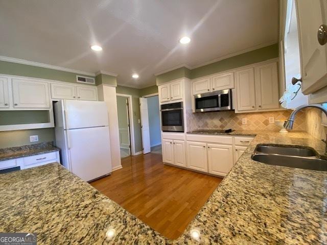 kitchen featuring sink, light hardwood / wood-style flooring, appliances with stainless steel finishes, white cabinetry, and tasteful backsplash