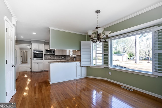 kitchen with tasteful backsplash, white cabinets, ornamental molding, kitchen peninsula, and stainless steel appliances