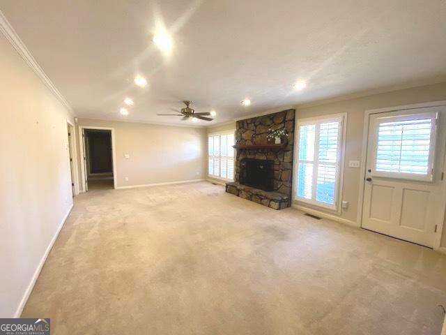 unfurnished living room with ceiling fan, ornamental molding, a fireplace, and carpet floors