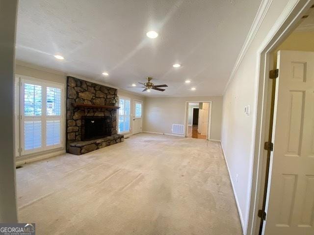 unfurnished living room with ornamental molding, a stone fireplace, a wealth of natural light, and light carpet