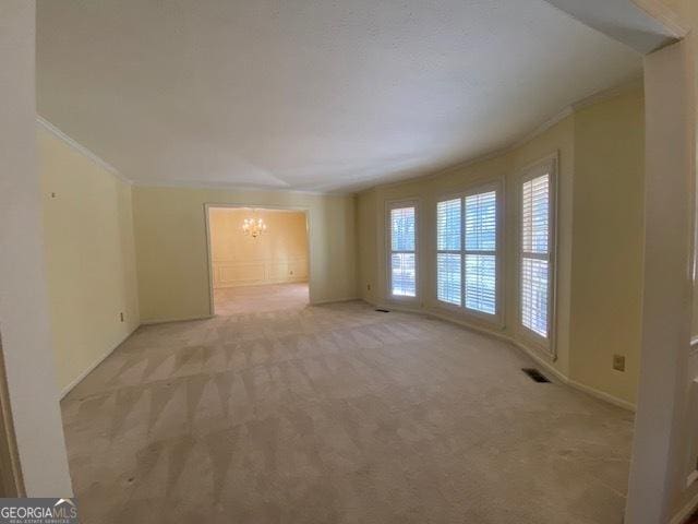 unfurnished room with ornamental molding, light carpet, and a chandelier