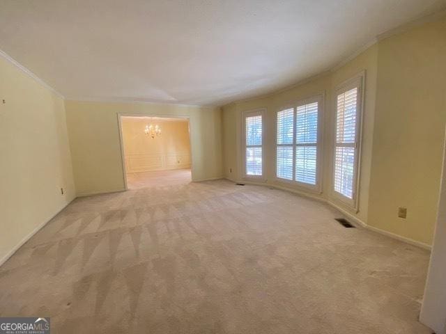 empty room with crown molding, light colored carpet, and a notable chandelier