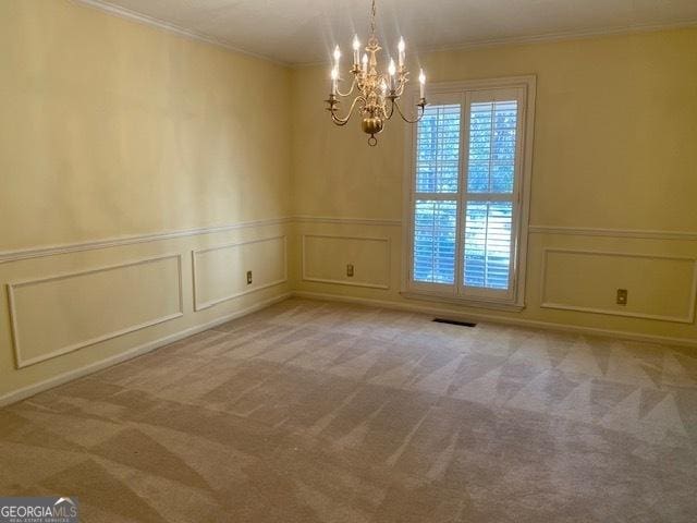 empty room with an inviting chandelier, ornamental molding, and light colored carpet