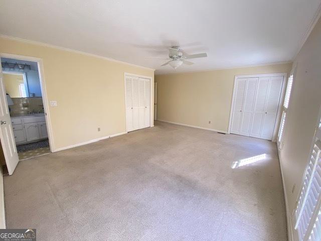 unfurnished bedroom with ensuite bathroom, crown molding, multiple closets, ceiling fan, and carpet