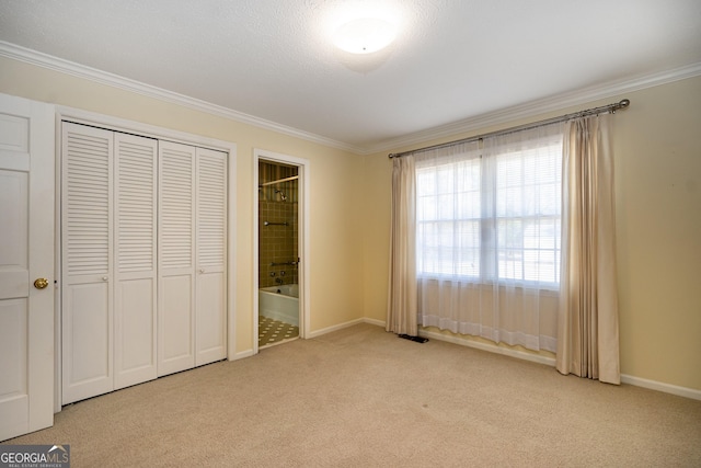 unfurnished bedroom with crown molding, a closet, ensuite bath, and light carpet