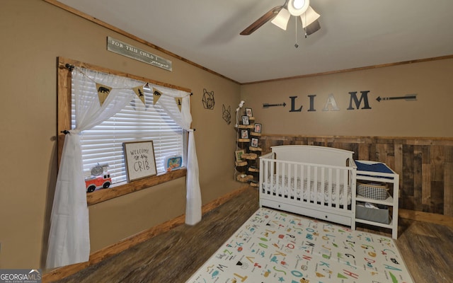 bedroom featuring dark wood-type flooring, ceiling fan, crown molding, and a crib