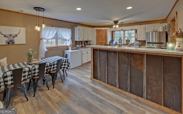 kitchen featuring stainless steel refrigerator, white cabinetry, ornamental molding, and decorative light fixtures