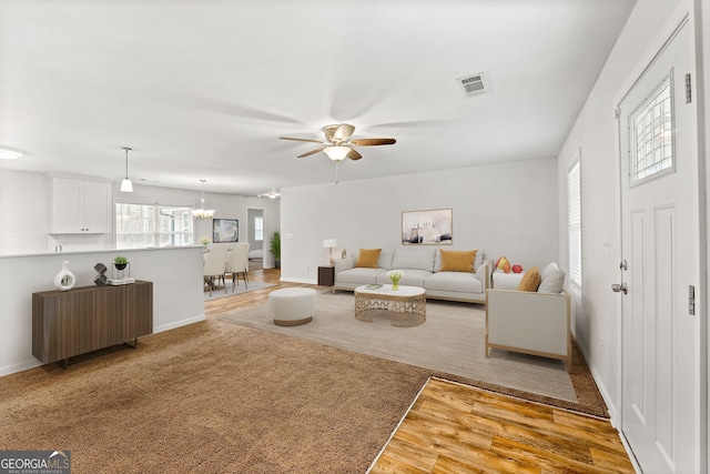 living room with ceiling fan with notable chandelier and light hardwood / wood-style floors