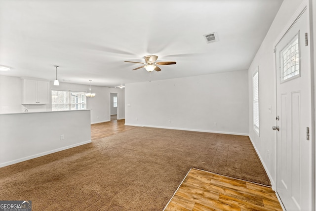 unfurnished living room with carpet flooring and ceiling fan with notable chandelier