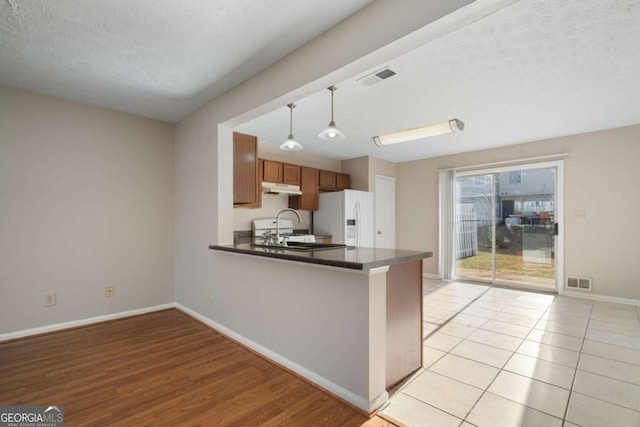 kitchen with sink, hanging light fixtures, white fridge with ice dispenser, kitchen peninsula, and a textured ceiling