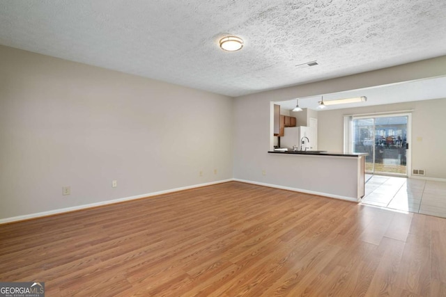 unfurnished living room featuring light hardwood / wood-style floors and a textured ceiling