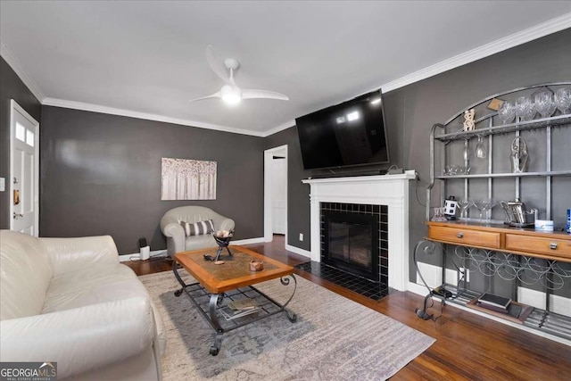 living room featuring a tiled fireplace, crown molding, dark hardwood / wood-style floors, and ceiling fan