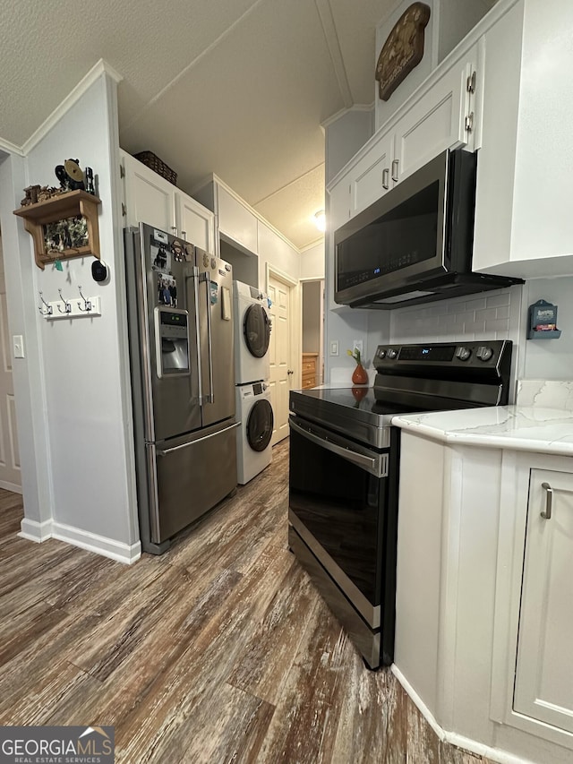 kitchen with stacked washing maching and dryer, appliances with stainless steel finishes, dark hardwood / wood-style floors, white cabinetry, and crown molding