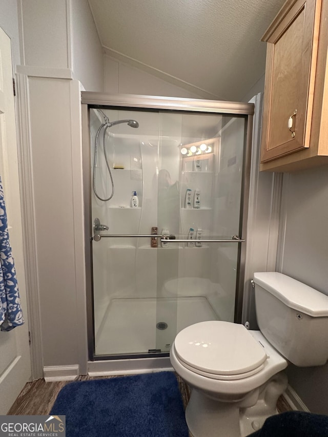 bathroom featuring a textured ceiling, vaulted ceiling, a shower with door, and toilet