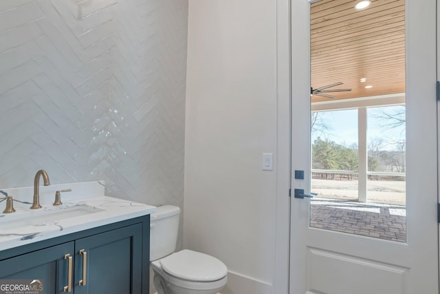 bathroom with ceiling fan, vanity, toilet, and tile walls