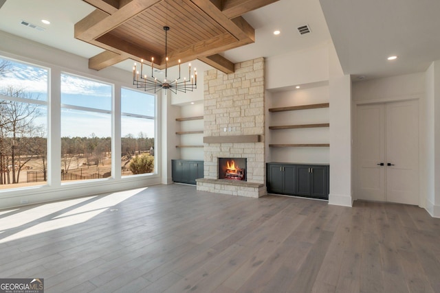 unfurnished living room featuring hardwood / wood-style flooring, a stone fireplace, an inviting chandelier, and beamed ceiling