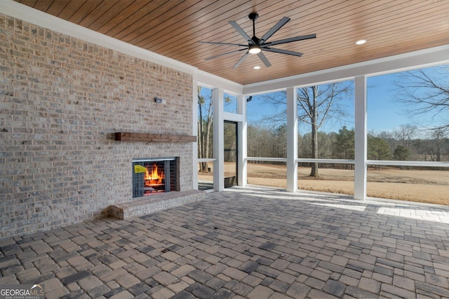 unfurnished sunroom featuring an outdoor brick fireplace, wood ceiling, a wealth of natural light, and ceiling fan