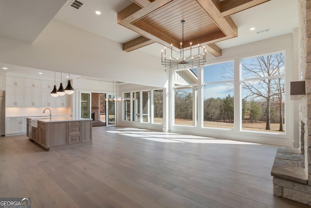 unfurnished living room with sink, a towering ceiling, a chandelier, beamed ceiling, and light wood-type flooring