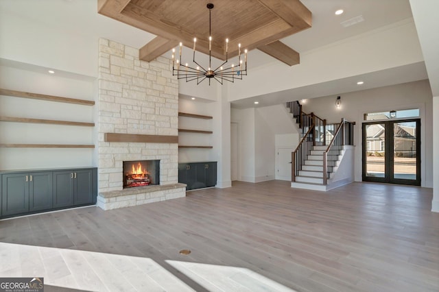 unfurnished living room with a fireplace, beamed ceiling, hardwood / wood-style flooring, a high ceiling, and an inviting chandelier