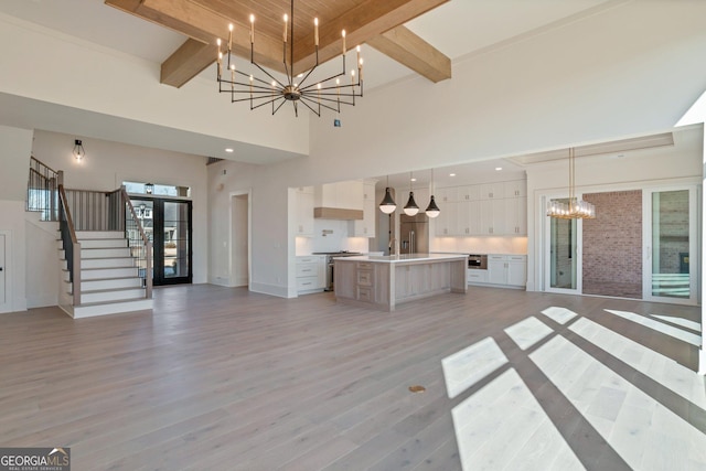 unfurnished living room featuring an inviting chandelier, beam ceiling, light hardwood / wood-style flooring, and a wealth of natural light