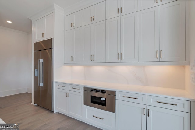 kitchen featuring light hardwood / wood-style flooring, built in appliances, tasteful backsplash, ornamental molding, and white cabinets