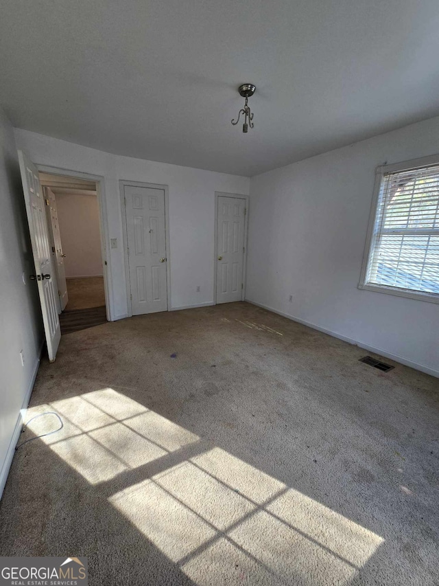 unfurnished bedroom featuring multiple closets and light colored carpet