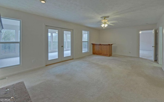 unfurnished living room with light carpet, ceiling fan, french doors, and a textured ceiling