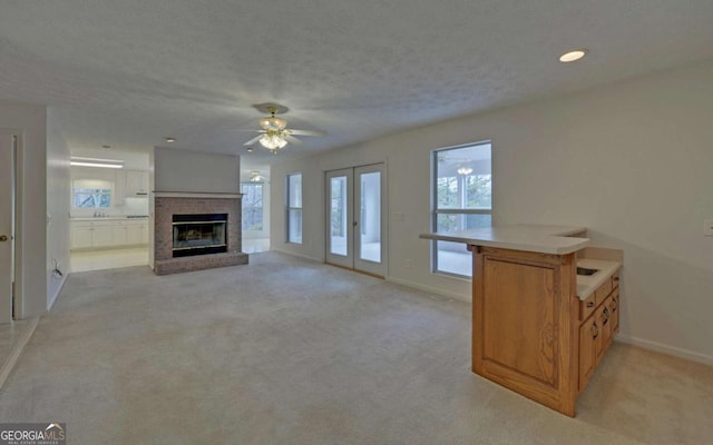 unfurnished living room with french doors, a brick fireplace, light carpet, and a textured ceiling