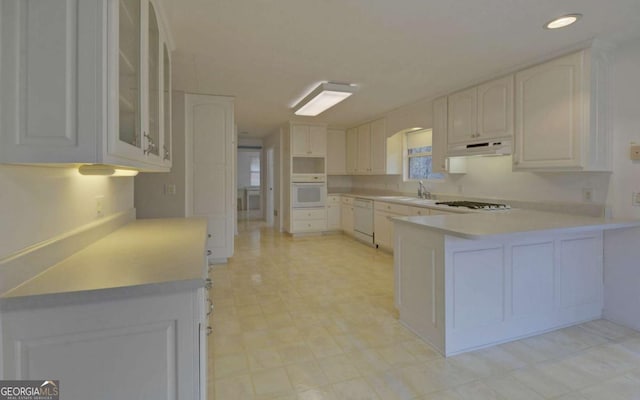 kitchen with sink, white appliances, kitchen peninsula, and white cabinets