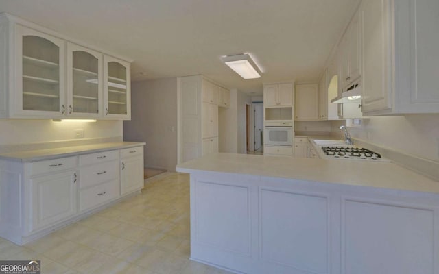 kitchen with white appliances, kitchen peninsula, and white cabinets