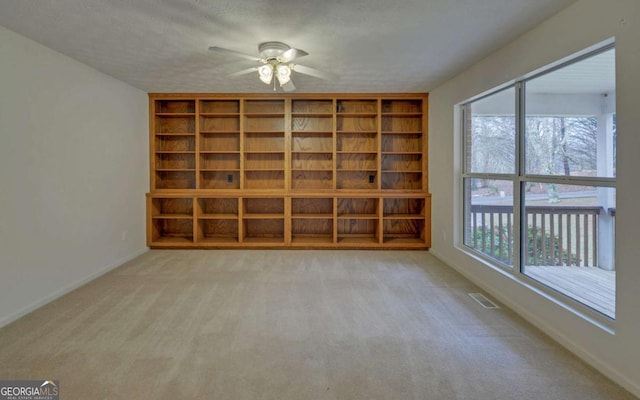 empty room with built in shelves, ceiling fan, light carpet, and a textured ceiling