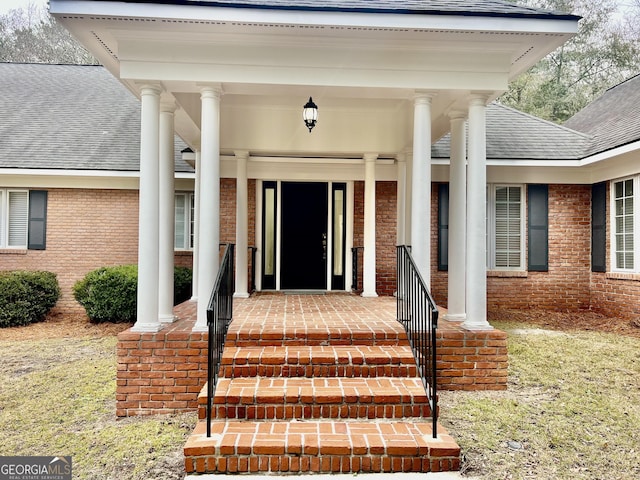 entrance to property with brick siding and a shingled roof