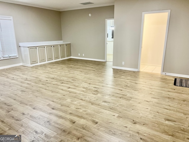 empty room featuring light wood finished floors, baseboards, and crown molding