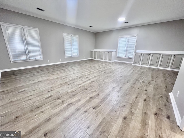 unfurnished room with baseboards, light wood-style flooring, visible vents, and crown molding