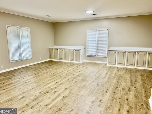 unfurnished room with ornamental molding, light wood-type flooring, visible vents, and baseboards