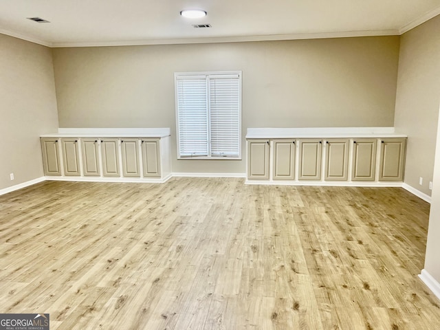 empty room featuring ornamental molding, light wood-type flooring, visible vents, and baseboards