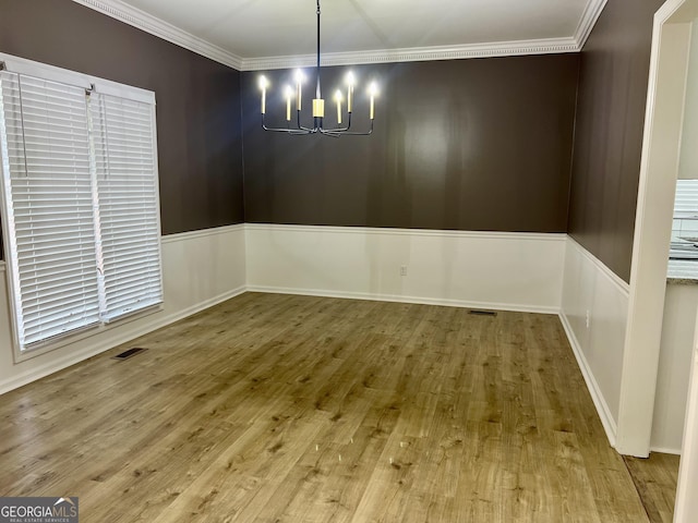 unfurnished dining area with ornamental molding, a chandelier, visible vents, and wood finished floors