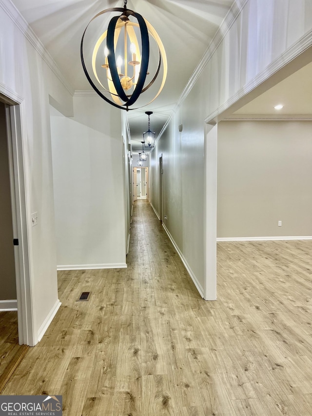 hall featuring a notable chandelier, light wood finished floors, baseboards, and crown molding