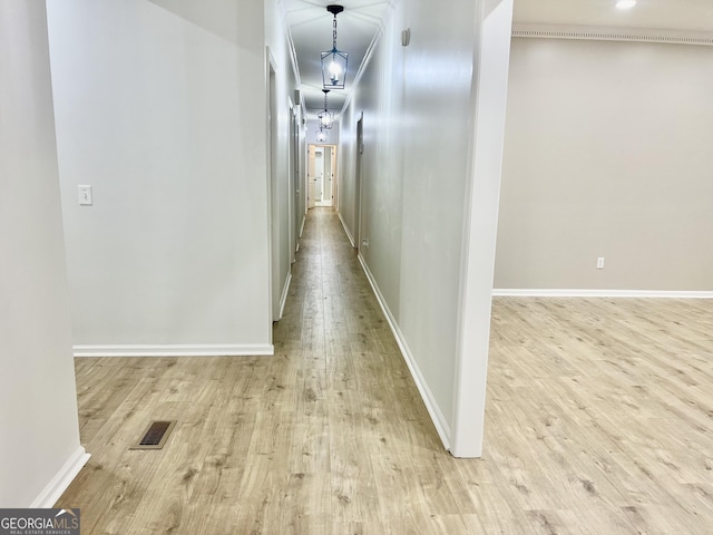 hall with light wood-type flooring, visible vents, and baseboards